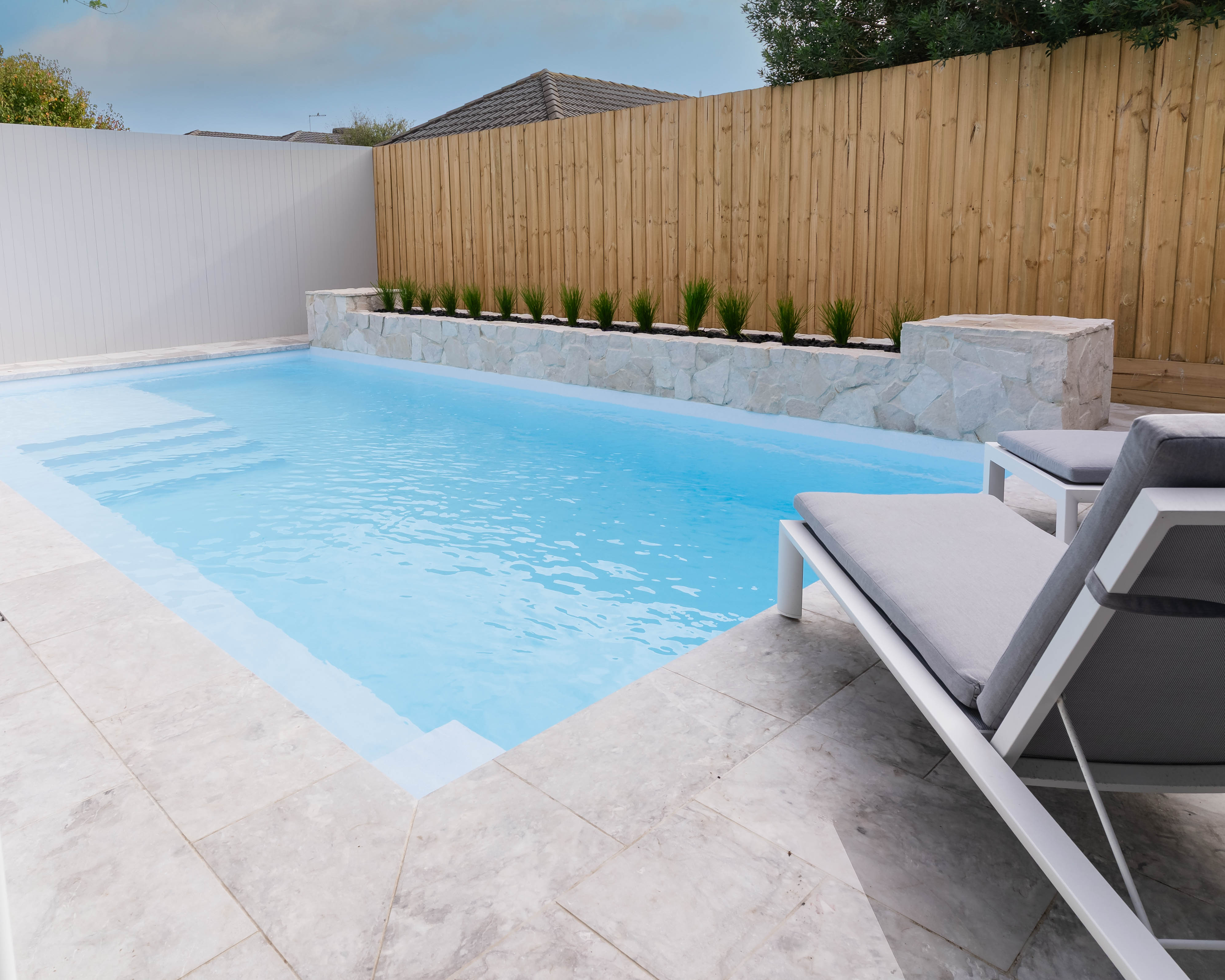 Sparkling blue swimming pool under Melbourne’s sunny sky, surrounded by modern outdoor lounge chairs.