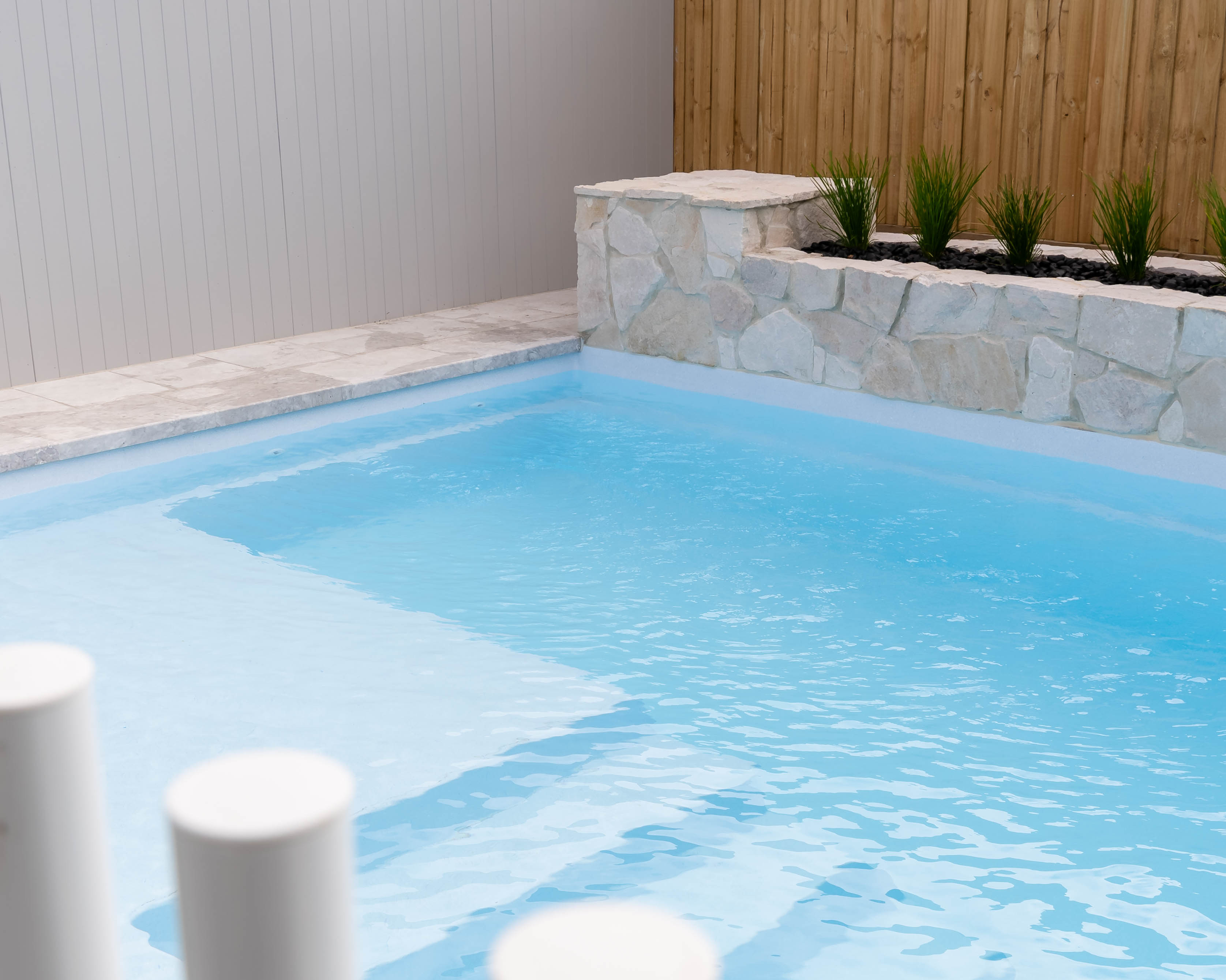 Textured stone pool coping surrounded by vibrant greenery, blending luxury landscaping with organic textures in Melbourne.